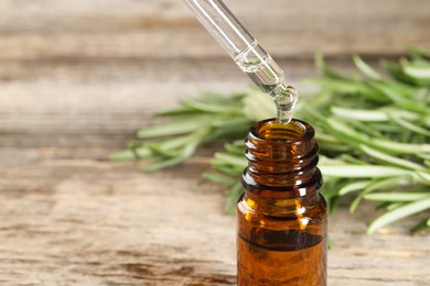 Photo of Dripping essential oil into bottle on wooden table, closeup