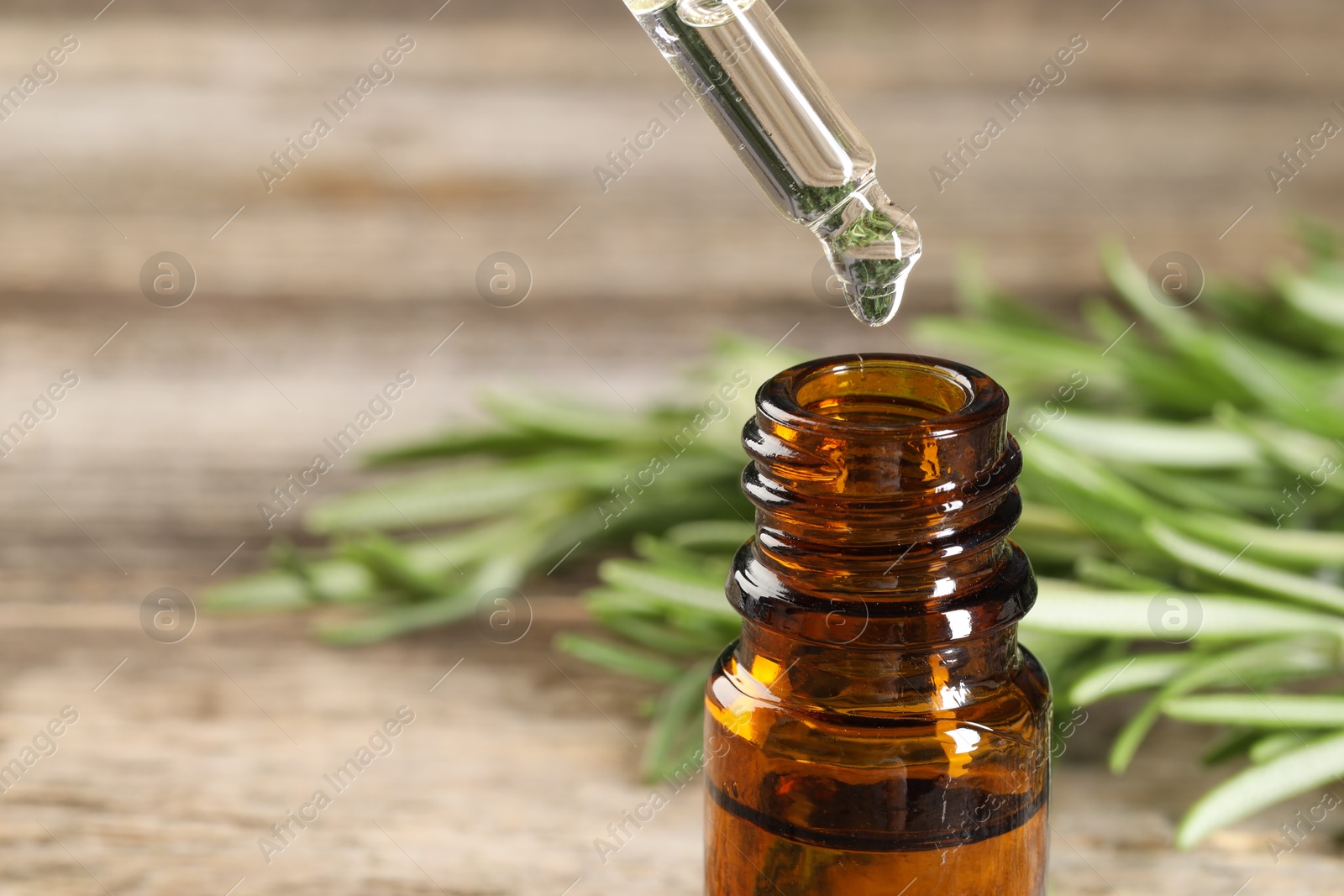 Photo of Dripping essential oil into bottle on wooden table, closeup