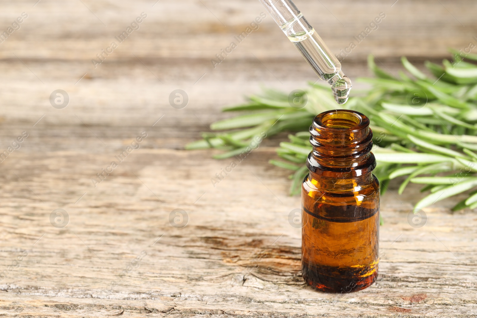 Photo of Dripping essential oil into bottle on wooden table, closeup. Space for text