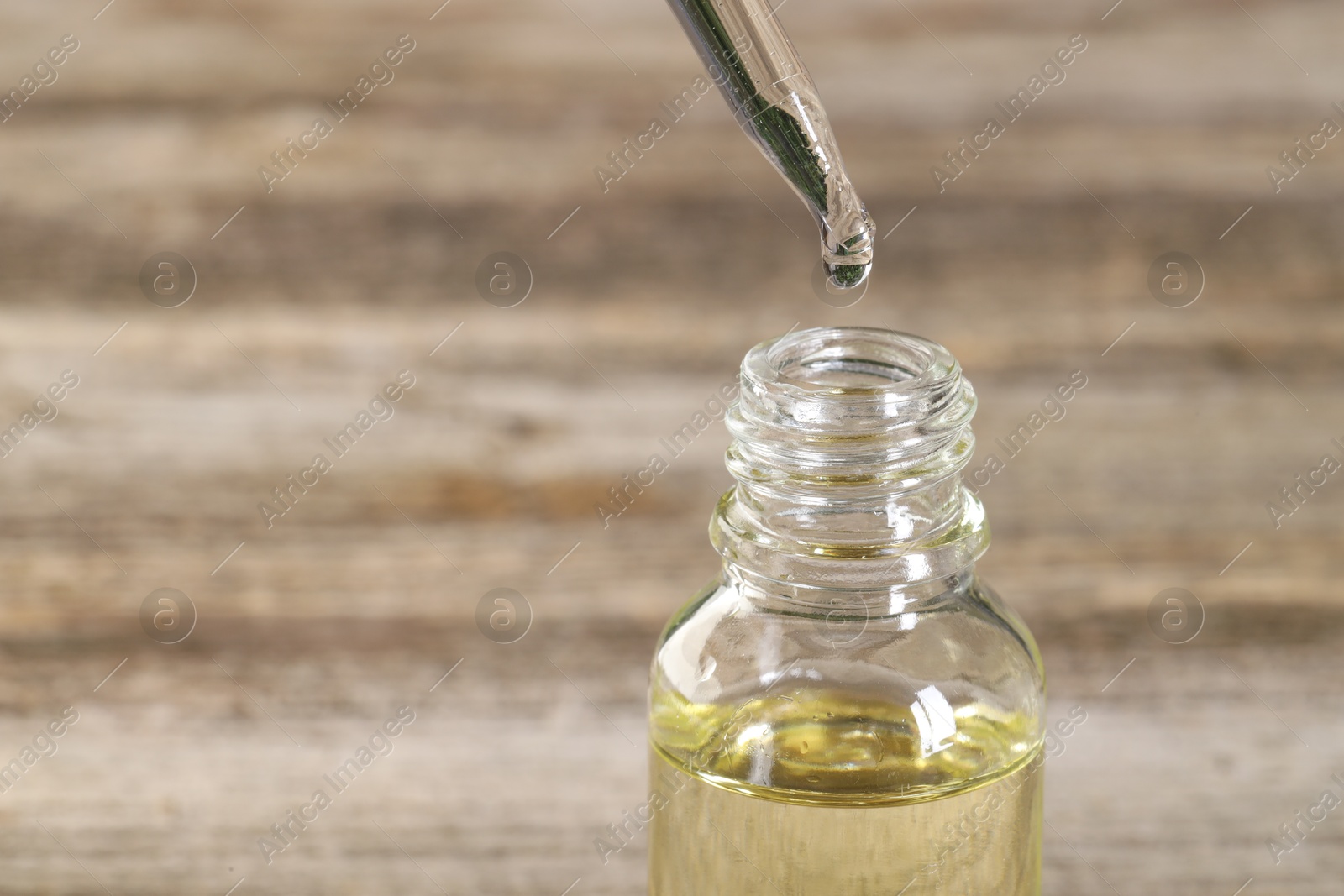 Photo of Dripping essential oil into bottle on wooden table, closeup. Space for text