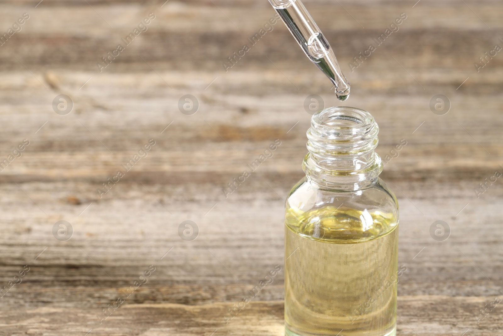 Photo of Dripping essential oil into bottle on wooden table, closeup. Space for text