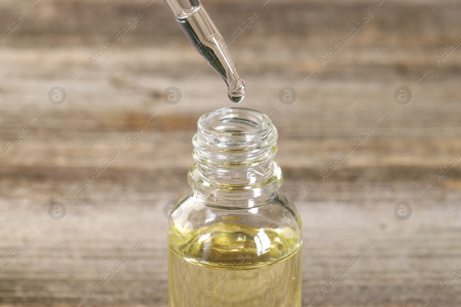 Photo of Dripping essential oil into bottle on wooden table, closeup