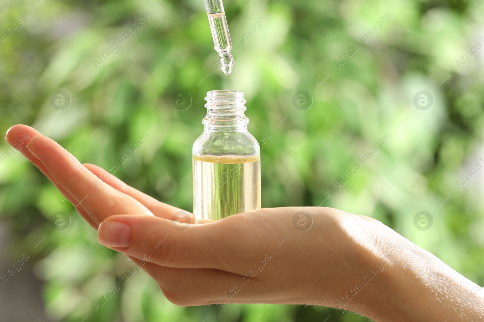 Photo of Woman dripping essential oil into bottle on blurred background, closeup