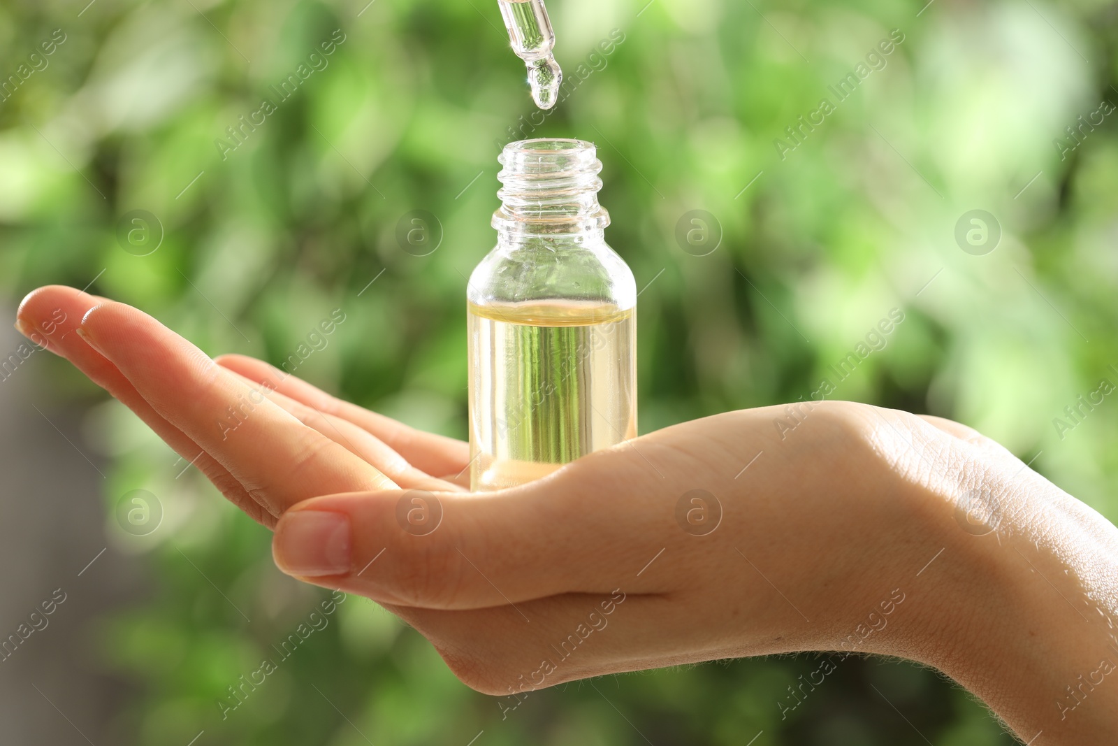 Photo of Woman dripping essential oil into bottle on blurred background, closeup