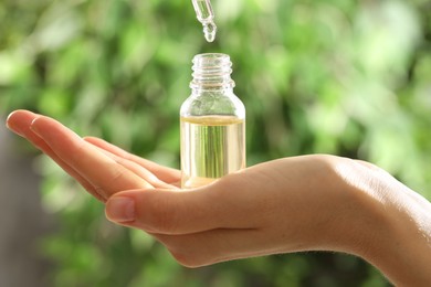 Photo of Woman dripping essential oil into bottle on blurred background, closeup