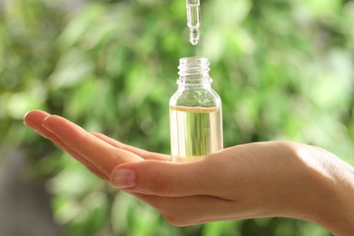 Photo of Woman dripping essential oil into bottle on blurred background, closeup