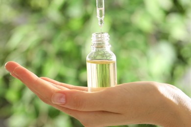 Photo of Woman dripping essential oil into bottle on blurred background, closeup