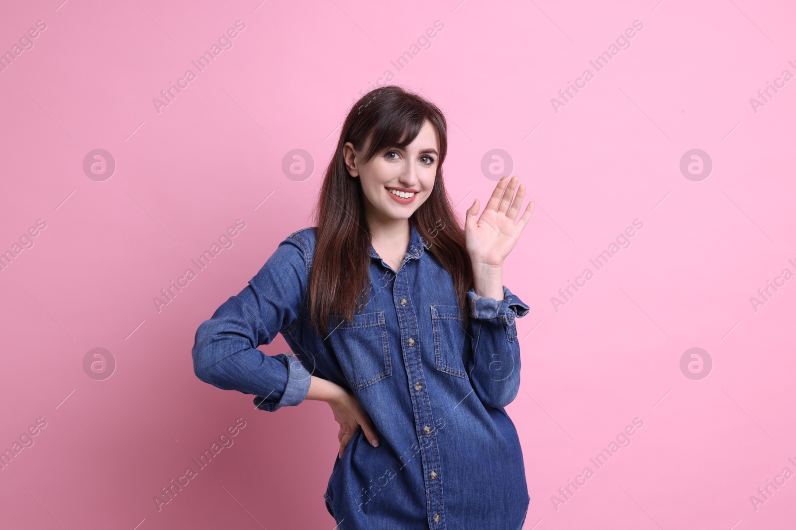 Photo of Happy young woman waving on pink background