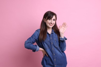 Happy young woman waving on pink background