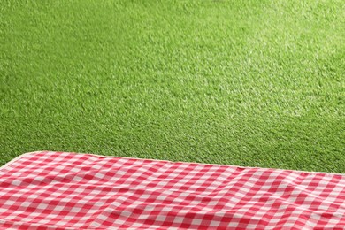 Photo of Checkered picnic tablecloth on green grass, closeup. Space for text