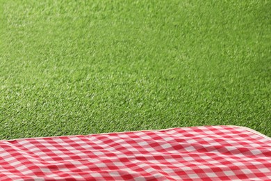 Photo of Checkered picnic tablecloth on green grass, closeup. Space for text