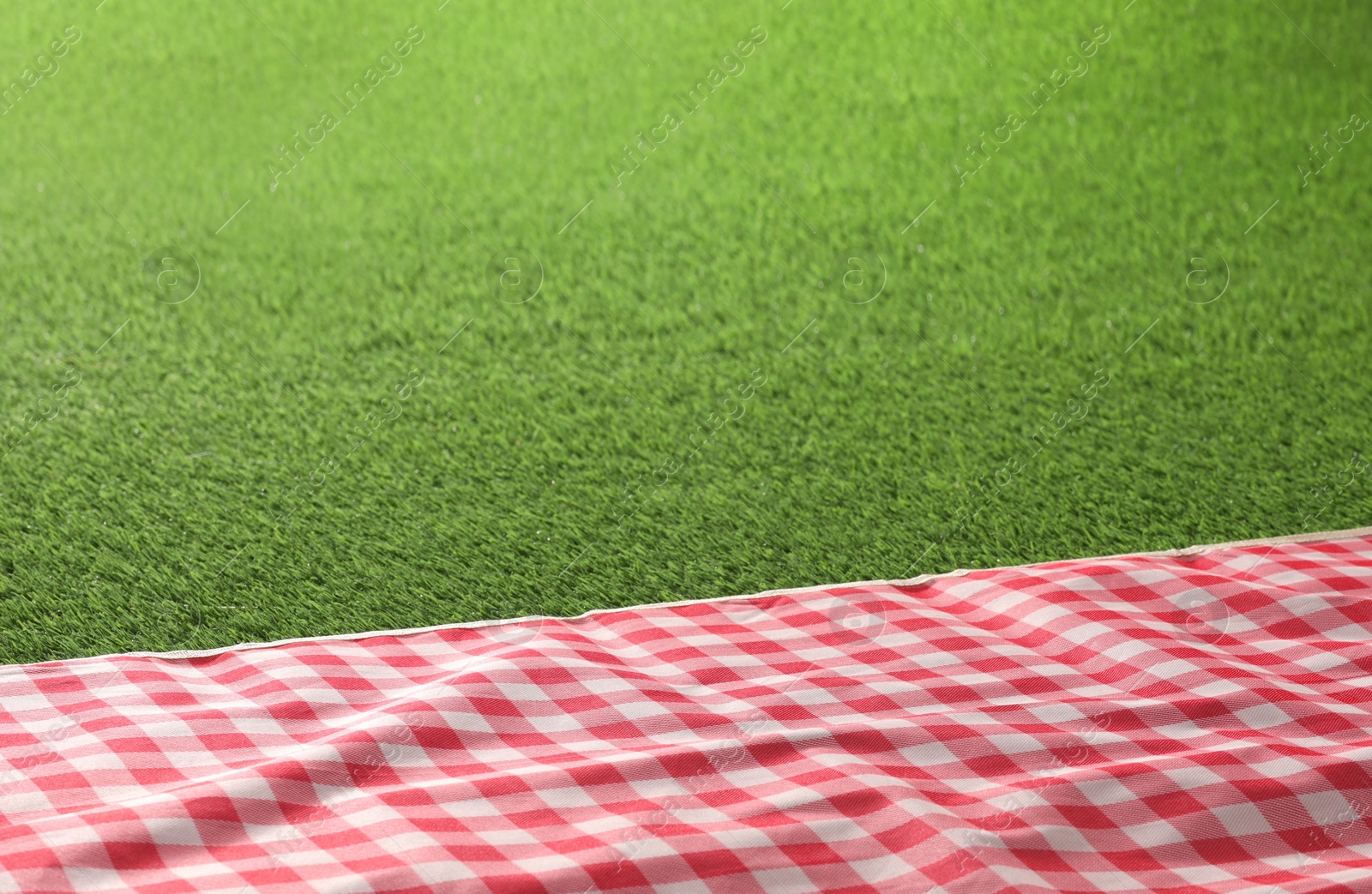 Photo of Checkered picnic tablecloth on green grass, closeup. Space for text