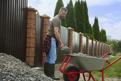 Man with shovel loading stones into wheelbarrow outdoors