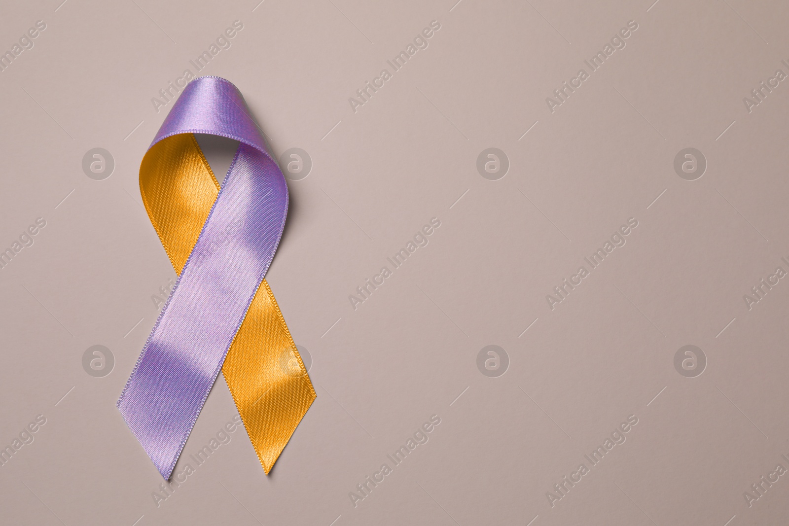 Image of World Psoriasis Day. Orange and orchid awareness ribbon as symbol of support on dark beige background, top view. Space for text