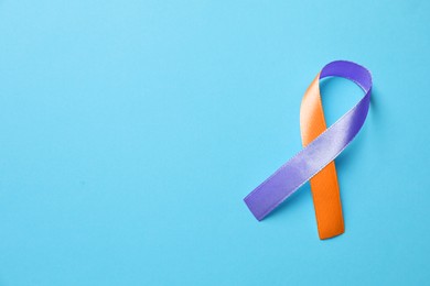 Image of World Psoriasis Day. Orange and orchid awareness ribbon as symbol of support on light blue background, top view. Space for text