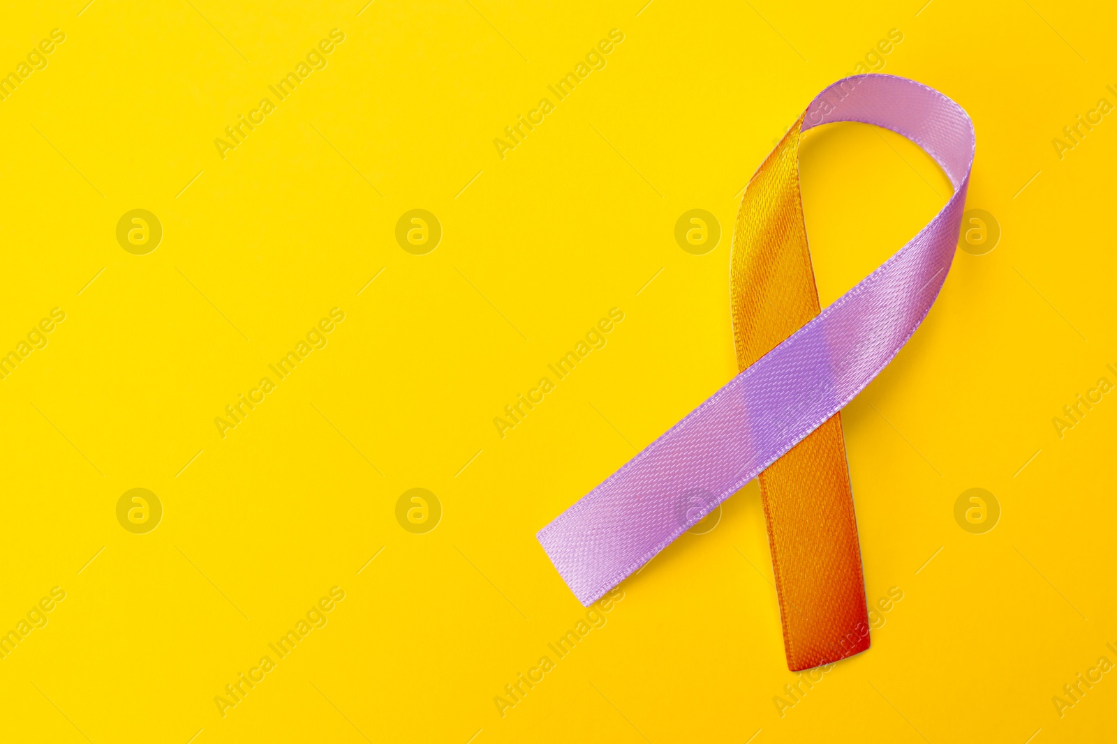 Image of World Psoriasis Day. Orange and orchid awareness ribbon as symbol of support on yellow background, top view. Space for text