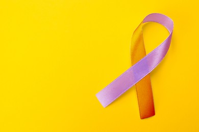 Image of World Psoriasis Day. Orange and orchid awareness ribbon as symbol of support on yellow background, top view. Space for text