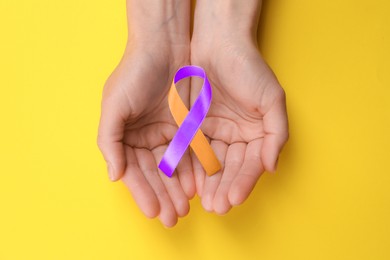 Image of World Psoriasis Day. Woman with orange and orchid ribbon as symbol of support on yellow background, top view