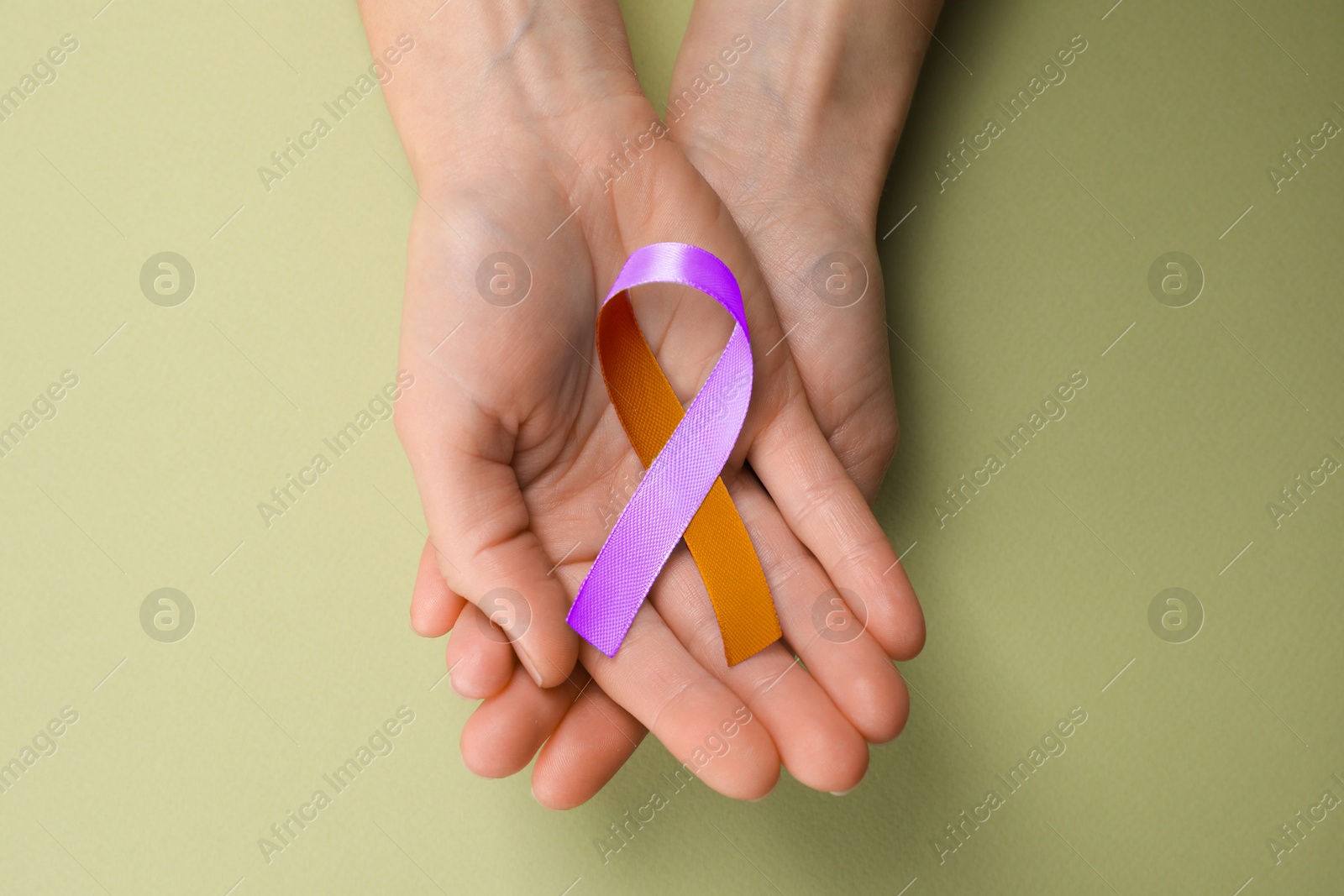 Image of World Psoriasis Day. Woman with orange and orchid ribbon as symbol of support on olive color background, top view