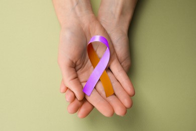 Image of World Psoriasis Day. Woman with orange and orchid ribbon as symbol of support on olive color background, top view