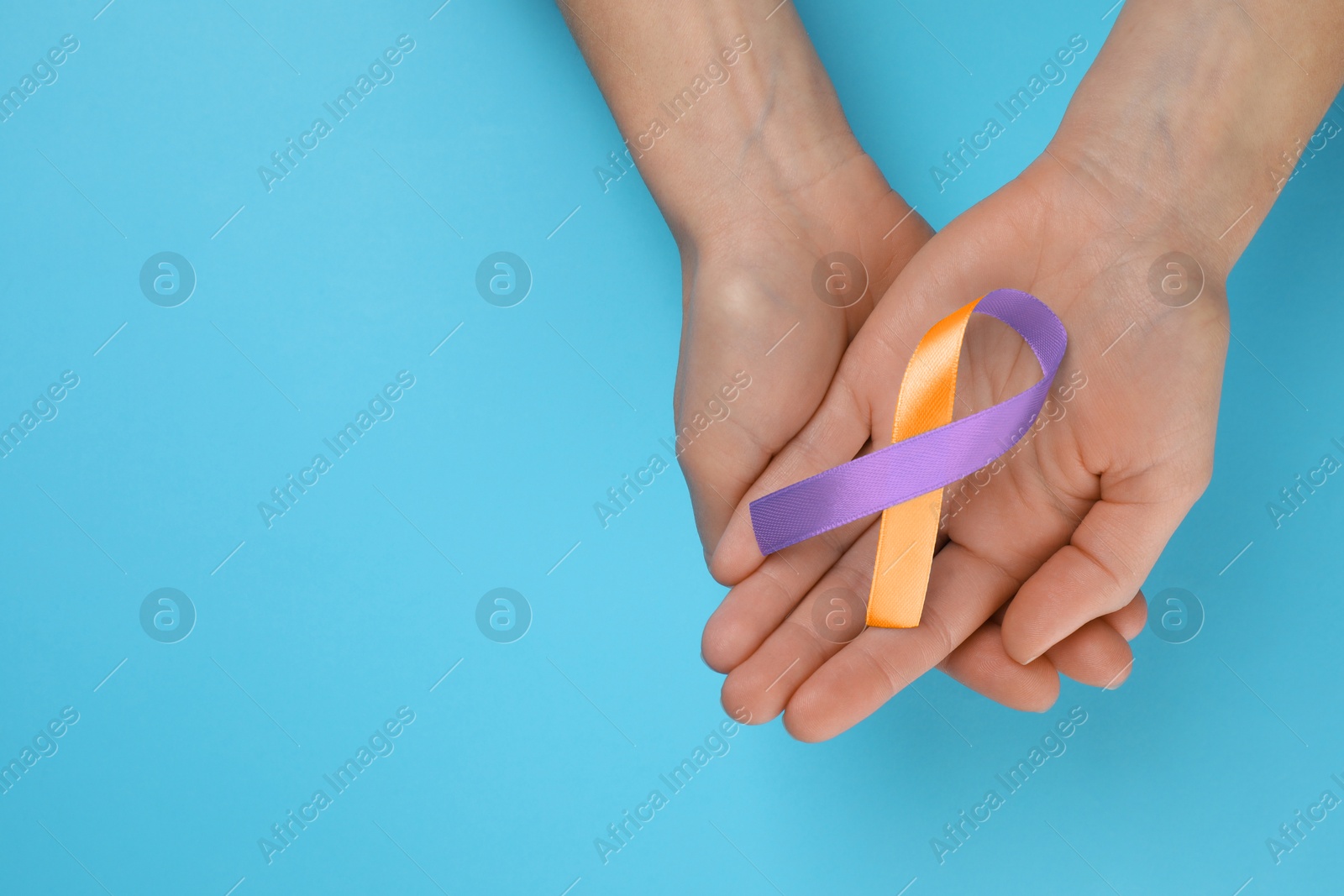 Image of World Psoriasis Day. Woman with orange and orchid ribbon as symbol of support on light blue background, top view. Space for text