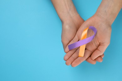 Image of World Psoriasis Day. Woman with orange and orchid ribbon as symbol of support on light blue background, top view. Space for text