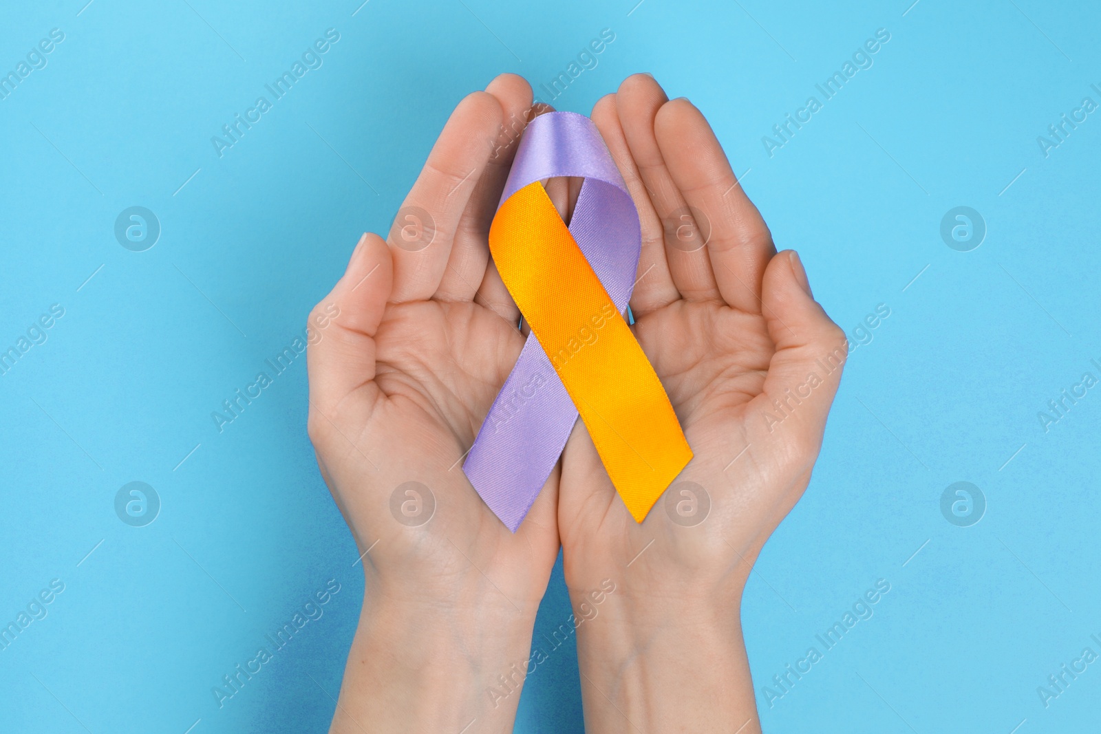 Image of World Psoriasis Day. Woman with orange and orchid ribbon as symbol of support on light blue background, top view