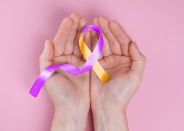 Image of World Psoriasis Day. Woman with orange and orchid ribbon as symbol of support on pink background, top view