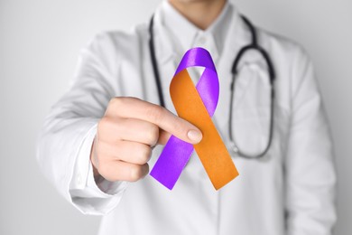 Image of World Psoriasis Day. Doctor with orange and orchid ribbon as symbol of support on white background, closeup