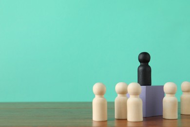 Photo of Black piece among wooden ones on table against turquoise background, space for text