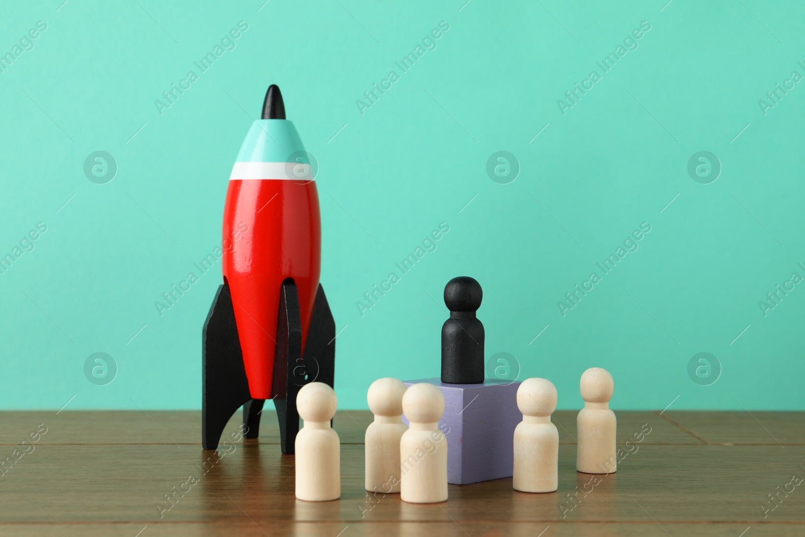 Photo of Black piece among wooden ones and rocket model on table against turquoise background