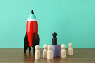 Photo of Black piece among wooden ones and rocket model on table against turquoise background