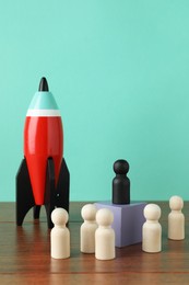 Black piece among wooden ones and rocket model on table against turquoise background