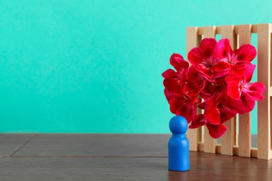 Blue human figure near beautiful flower on wooden table against turquoise background, space for text