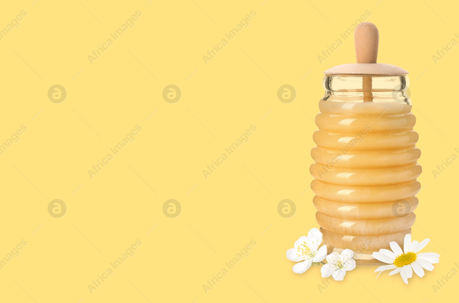 Image of Organic honey in glass jar and flowers on light golden background. Space for text