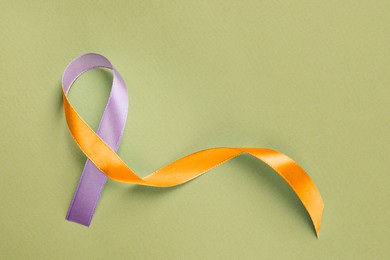 Image of World Psoriasis Day. Orange and orchid awareness ribbon as symbol of support on olive color background, top view. Space for text