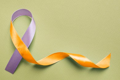 World Psoriasis Day. Orange and orchid awareness ribbon as symbol of support on olive color background, top view. Space for text