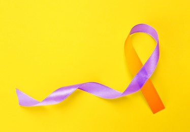 Image of World Psoriasis Day. Orange and orchid awareness ribbon as symbol of support on yellow background, top view. Space for text