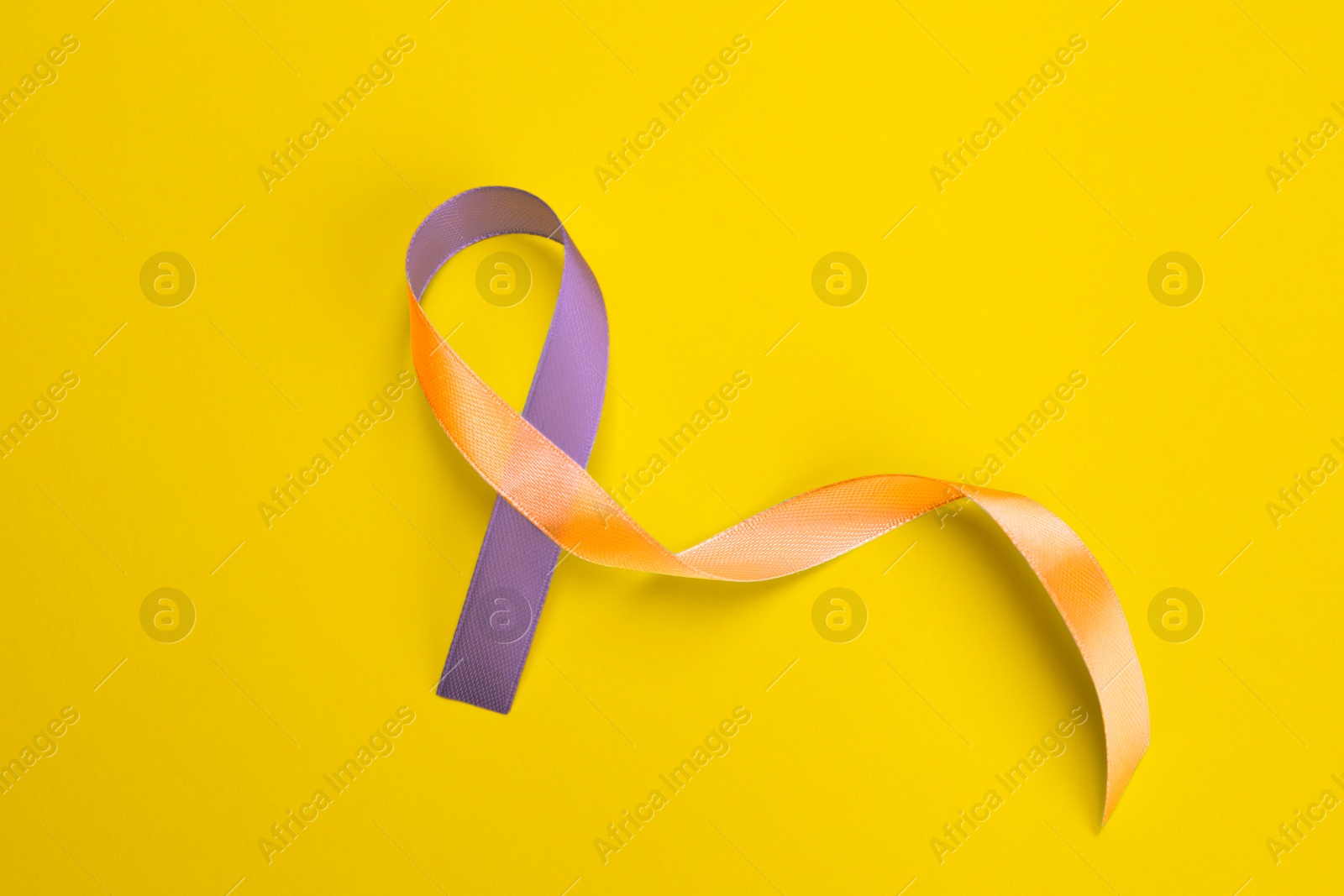 Image of World Psoriasis Day. Orange and orchid awareness ribbon as symbol of support on yellow background, top view