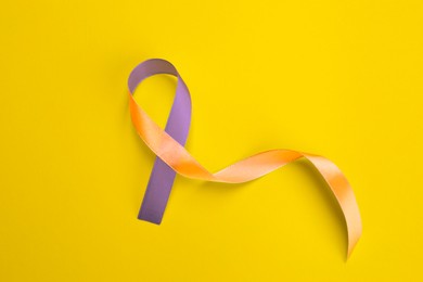 World Psoriasis Day. Orange and orchid awareness ribbon as symbol of support on yellow background, top view