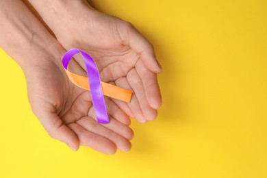 Image of World Psoriasis Day. Woman with orange and orchid ribbon as symbol of support on yellow background, top view. Space for text