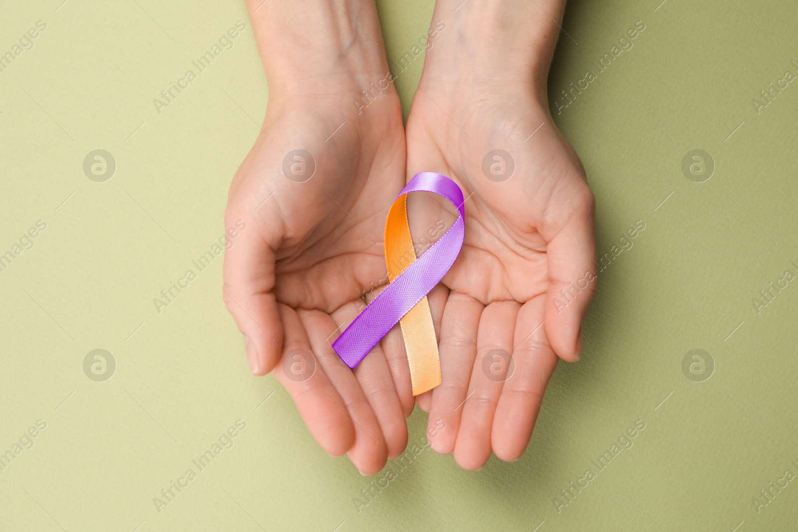 Image of World Psoriasis Day. Woman with orange and orchid ribbon as symbol of support on olive color background, top view