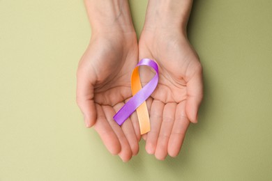 World Psoriasis Day. Woman with orange and orchid ribbon as symbol of support on olive color background, top view