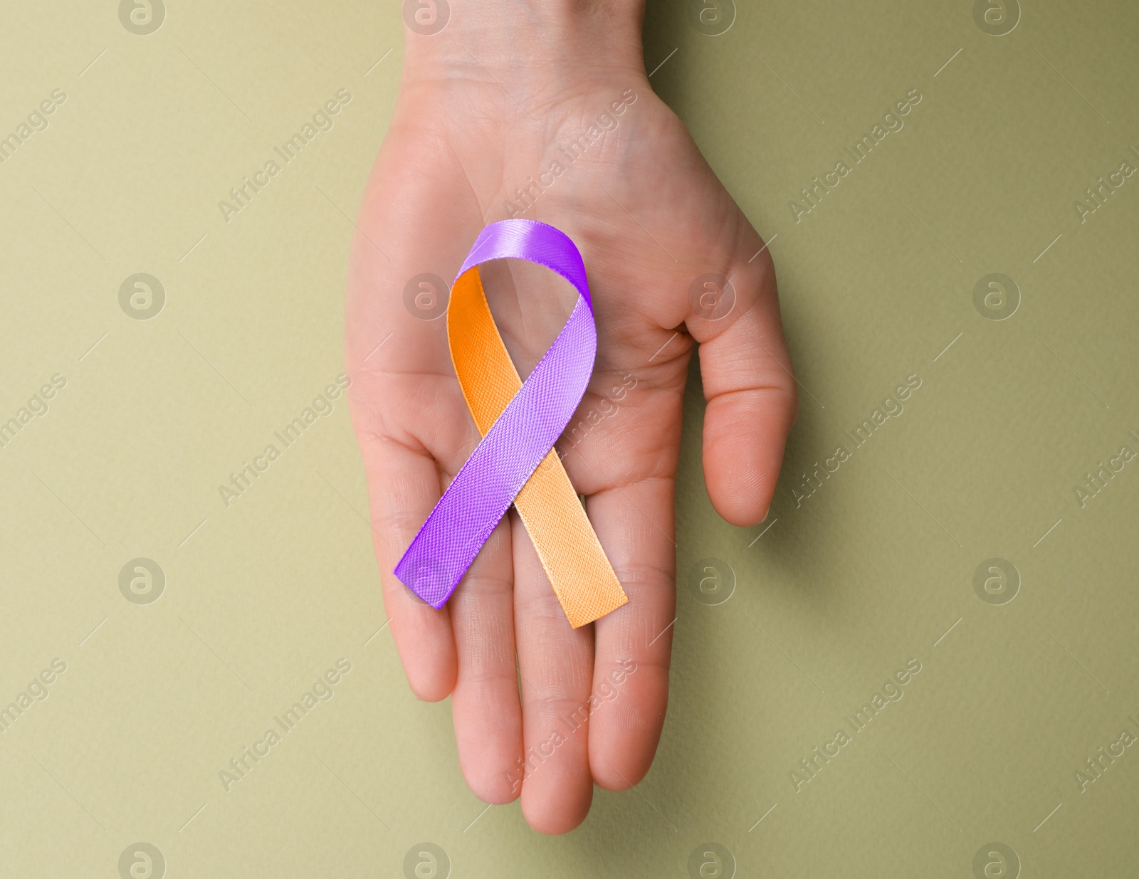 Image of World Psoriasis Day. Woman with orange and orchid ribbon as symbol of support on olive color background, top view