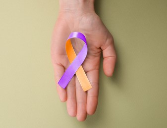 Image of World Psoriasis Day. Woman with orange and orchid ribbon as symbol of support on olive color background, top view