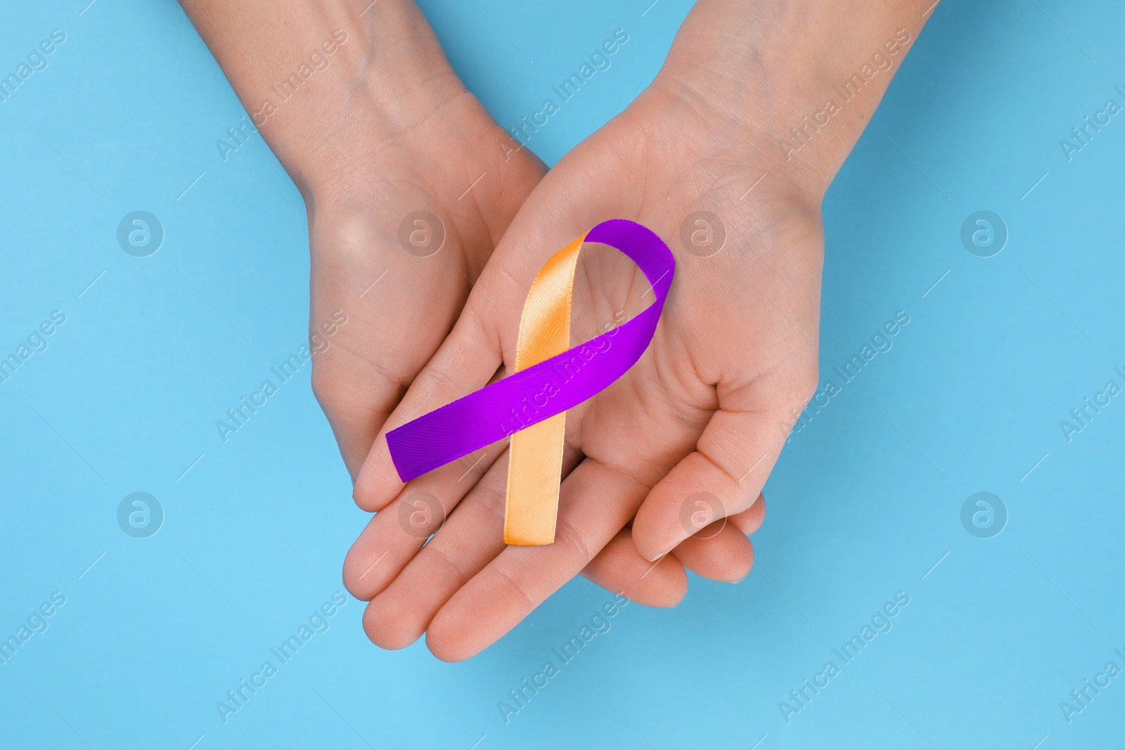 Image of World Psoriasis Day. Woman with orange and orchid ribbon as symbol of support on light blue background, top view