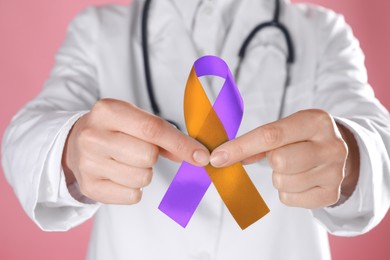 Image of World Psoriasis Day. Doctor with orange and orchid ribbon as symbol of support on pink background, closeup