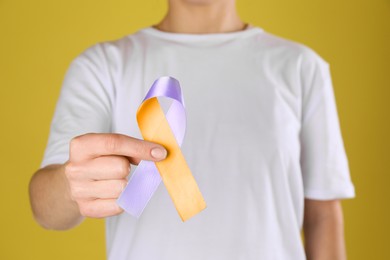 Image of World Psoriasis Day. Woman with orange and orchid ribbon as symbol of support on yellow background, closeup