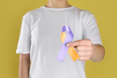 Image of World Psoriasis Day. Woman with orange and orchid ribbon as symbol of support on yellow background, closeup