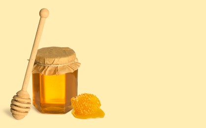 Image of Organic honey in glass jar, wooden dipper and honeycomb on beige background. Space for text